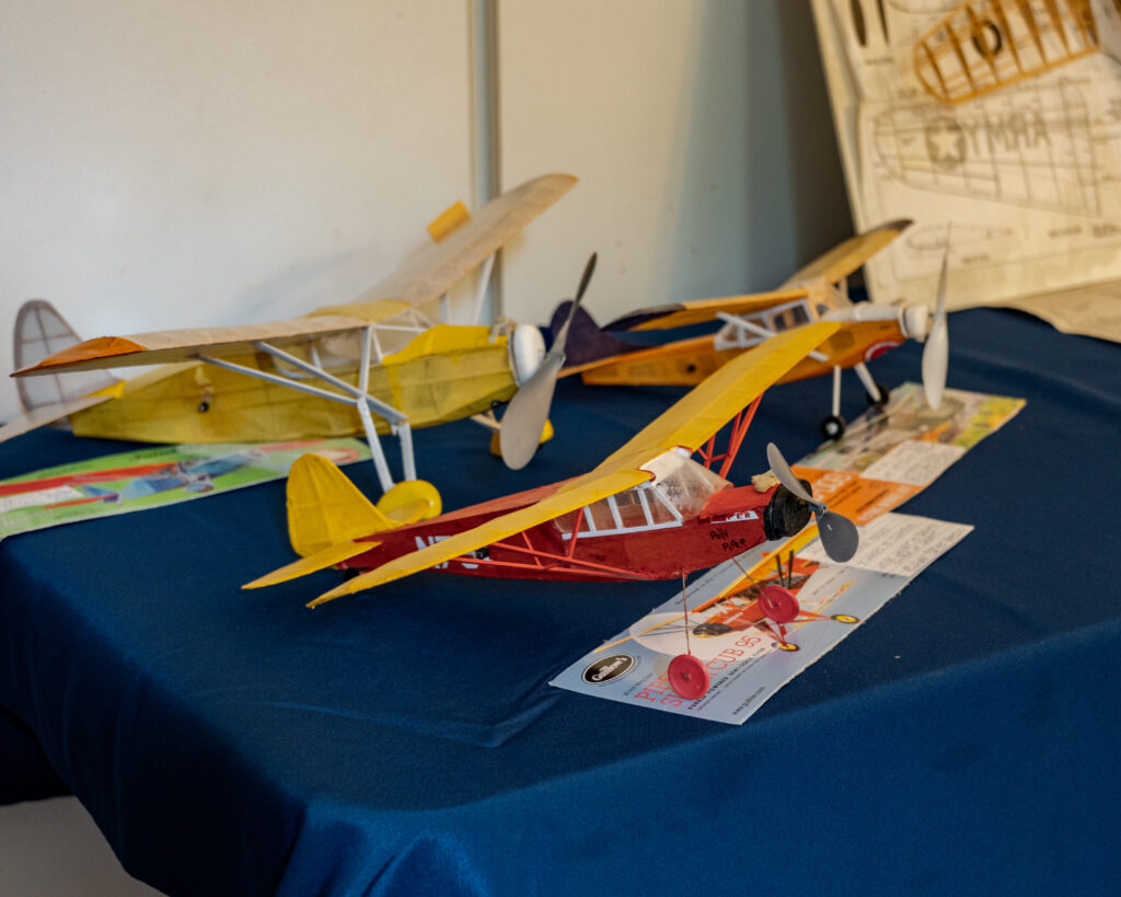 Model planes displayed on a blue tablecloth, showcasing vibrant red, yellow, and beige designs with propellers.