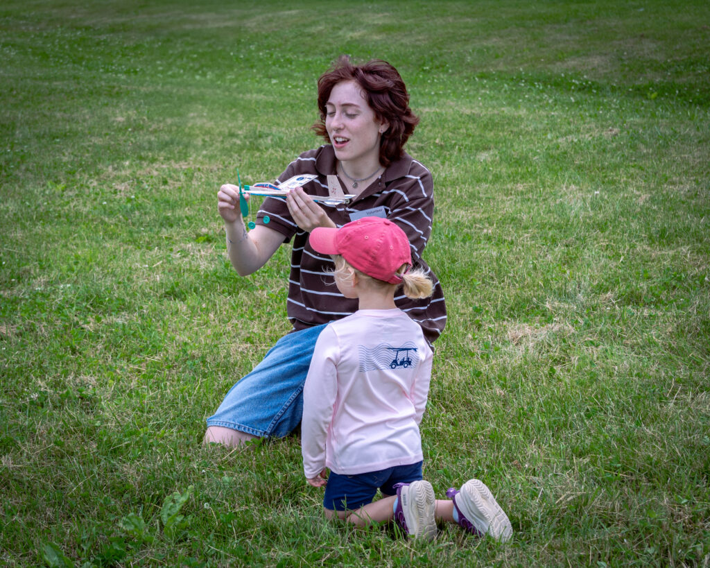 Person with child shows toy plane on lush green grass.
