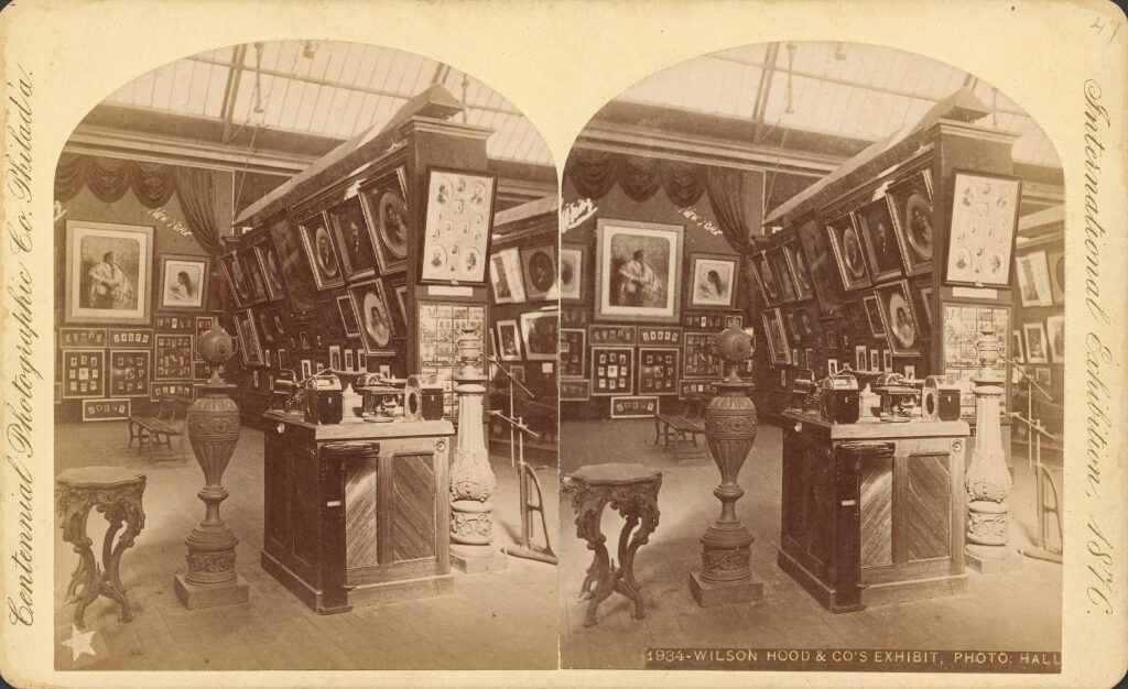 Victorian exhibition space filled with framed portraits and ornate vases. Wooden floors and a grand skylight above.