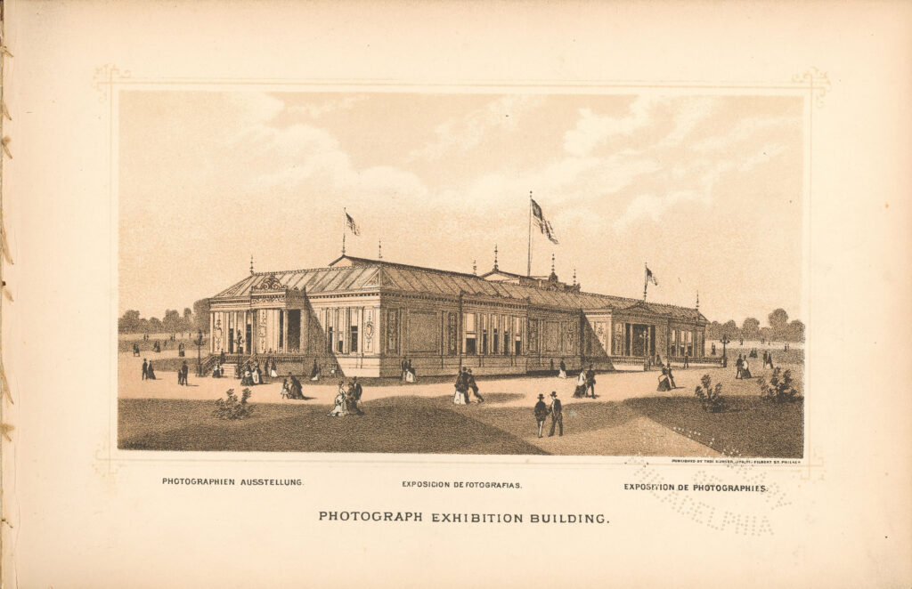 Victorian-era photograph exhibition building with ornate details, flags, and visitors strolling in a scenic setting.