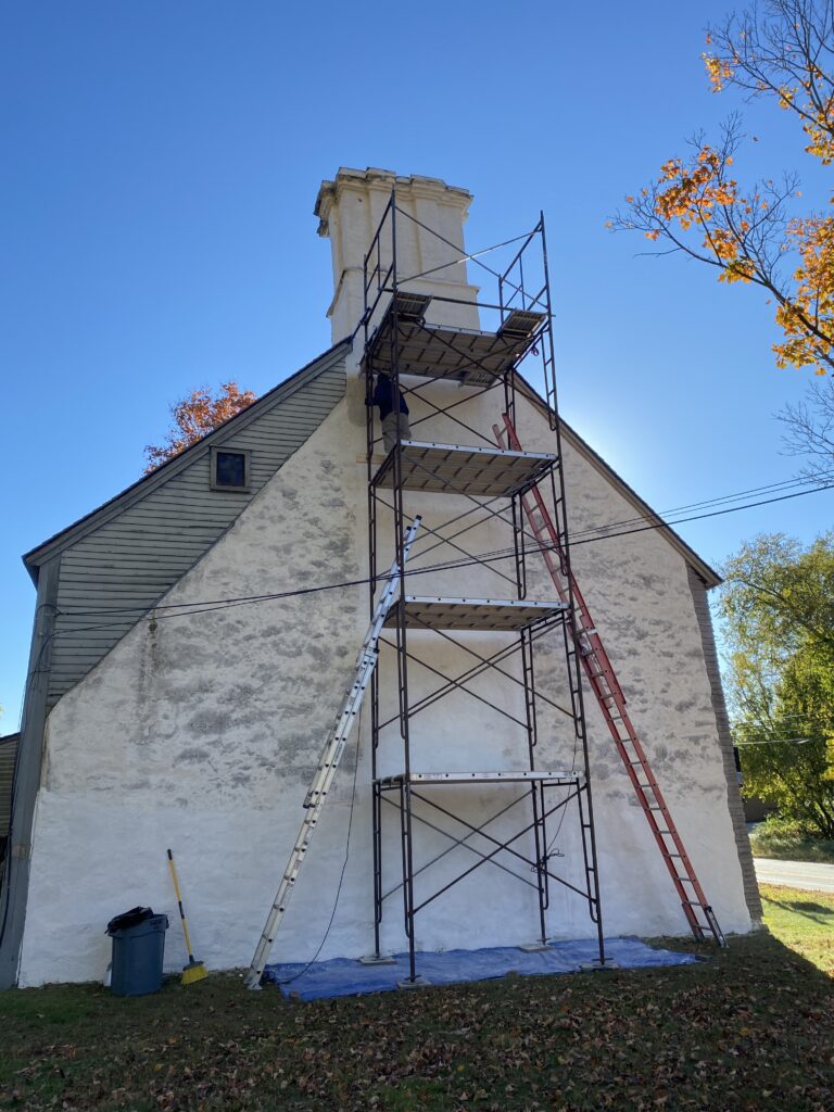 Historic house with scaffolding set up for chimney restoration under a clear blue sky. Autumn leaves add a touch of color.