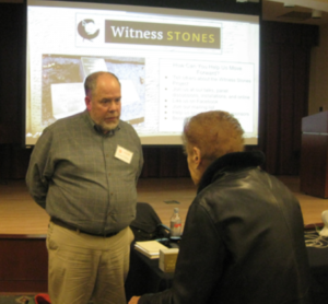 Man discussing the Witness Stones Project, presentation in the background.