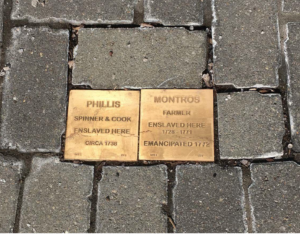 Gold plaques on cobblestones honoring Phillis and Montros, acknowledging their enslavement and commemorating emancipation.
