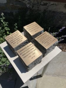 Brass memorial plaques honoring enslaved individuals on a stone pedestal in a garden setting.