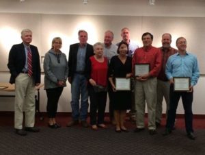 Group photo of ten people, some holding certificates, standing indoors against a white wall.