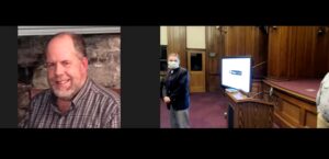 Split-screen video call with smiling man at home and masked person in an empty conference room with presentation screen.