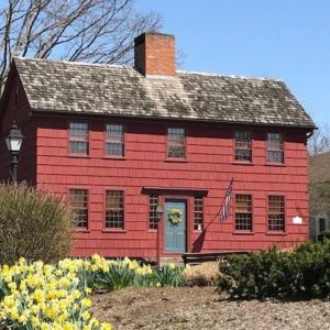 Historic red brick colonial house with American flag, daffodils, and clear blue sky, symbolizing rustic American charm.