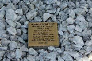 Memorial plaque for Nimrod Benedict on gray stones, detailing his life journey from enslavement to freedom.