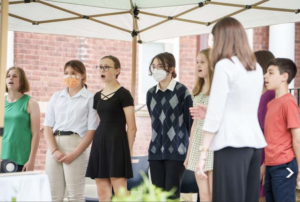 Group of students singing under a canopy during a choir performance outdoors.