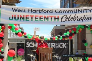 Juneteenth celebration at West Hartford with a speaker under a festive banner and colorful balloons.