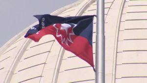 Flag with red, white, and blue colors featuring a star design, waving on a pole against a dome structure background.