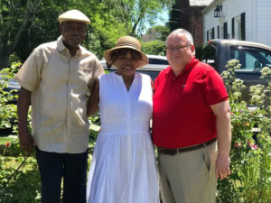 Three people smiling outside a house, standing together in a garden on a sunny day.