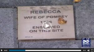 Memorial plaque for Rebecca, enslaved in 1736, located on site. Includes video timestamp and news watermark.