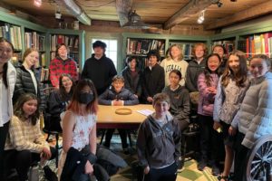Group of students meeting in a cozy library room, surrounded by bookshelves and smiling at the camera.