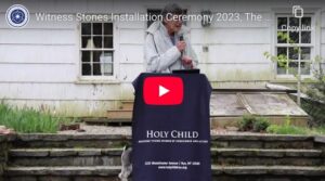 Person speaking at Holy Child's Witness Stones Installation Ceremony 2023, standing outdoors with greenery.