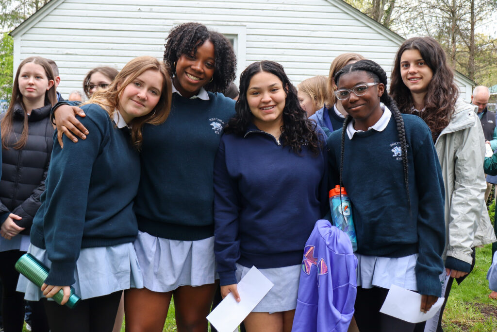 Group of smiling students in school uniforms outdoors, standing together and holding papers.