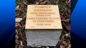 Plaque honoring Pompey, last known enslaved person in Guilford, carpenter, died 1819. Historical remembrance site.