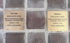 Brass plaques on brick sidewalk memorialize enslaved individuals, Peter and Dinah, sold in 1740 with unknown fates.