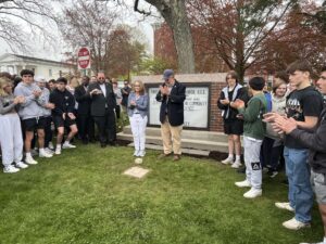 Group gathered outdoors by church sign, applauding and celebrating an event or announcement on a grassy area.