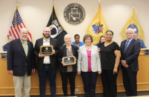 Group of people receiving awards in a ceremony at Somerset County, NJ, with flags displayed in the background.