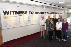 People standing in front of an exhibit titled Witness to History: Slavery in Guilford at a museum.