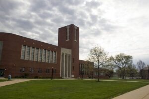 Modern brick building on campus with cloudy sky and green lawn.