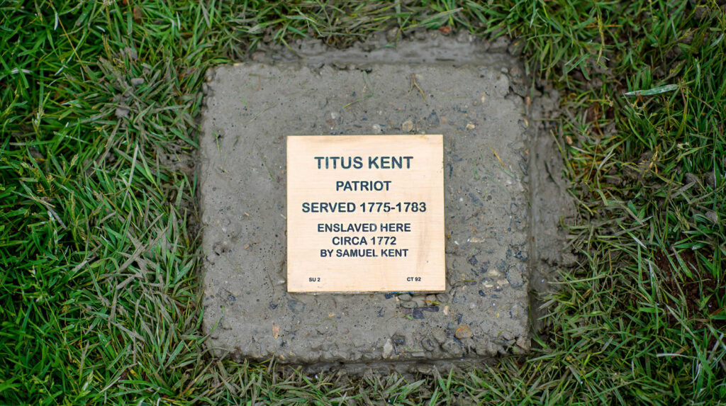Plaque honoring Titus Kent, Patriot served 1775-1783, enslaved circa 1772, surrounded by grass.