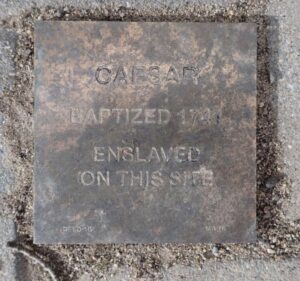 Plaque commemorating Caesar, baptized 1741, enslaved on this site, highlighting historical significance.