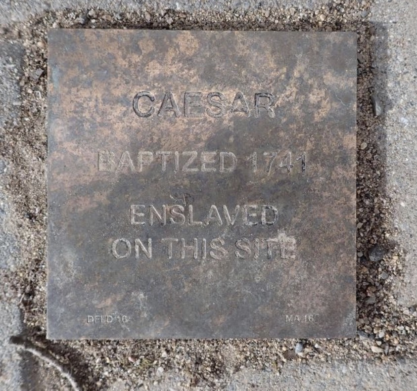 Plaque commemorating Caesar, baptized 1741, enslaved on this site, highlighting historical significance.