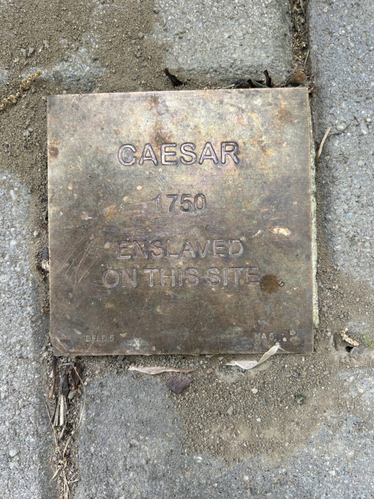 Bronze plaque on pavement marking historical site where Caesar was enslaved in 1750.