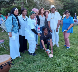 Group of people outdoors gathered for a community event, with one person crouched holding a small plaque.