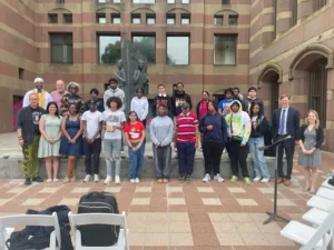 Group photo of diverse individuals standing in front of a historic building, smiling at an outdoor event.