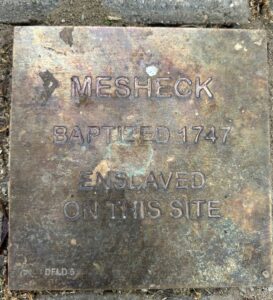 Historic plaque for Mesheck, baptized 1747, marking site of enslavement. A reminder of past injustices.