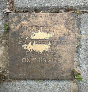 Bronze plaque commemorating Peter, baptized 1735, enslaved at this location. Historic remembrance on a sidewalk.