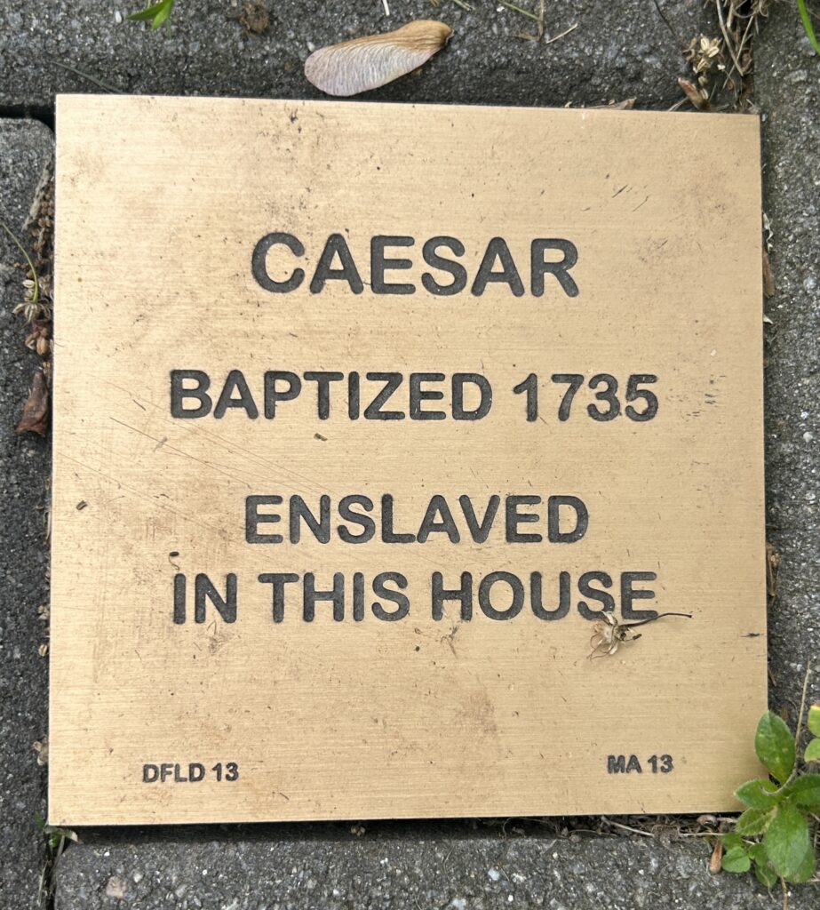 Memorial plaque honoring Caesar, baptized in 1735 and enslaved in the house, set in stone pavement.