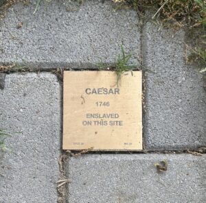 Commemorative plaque on pavement for Caesar, enslaved in 1746, highlighting historical site.