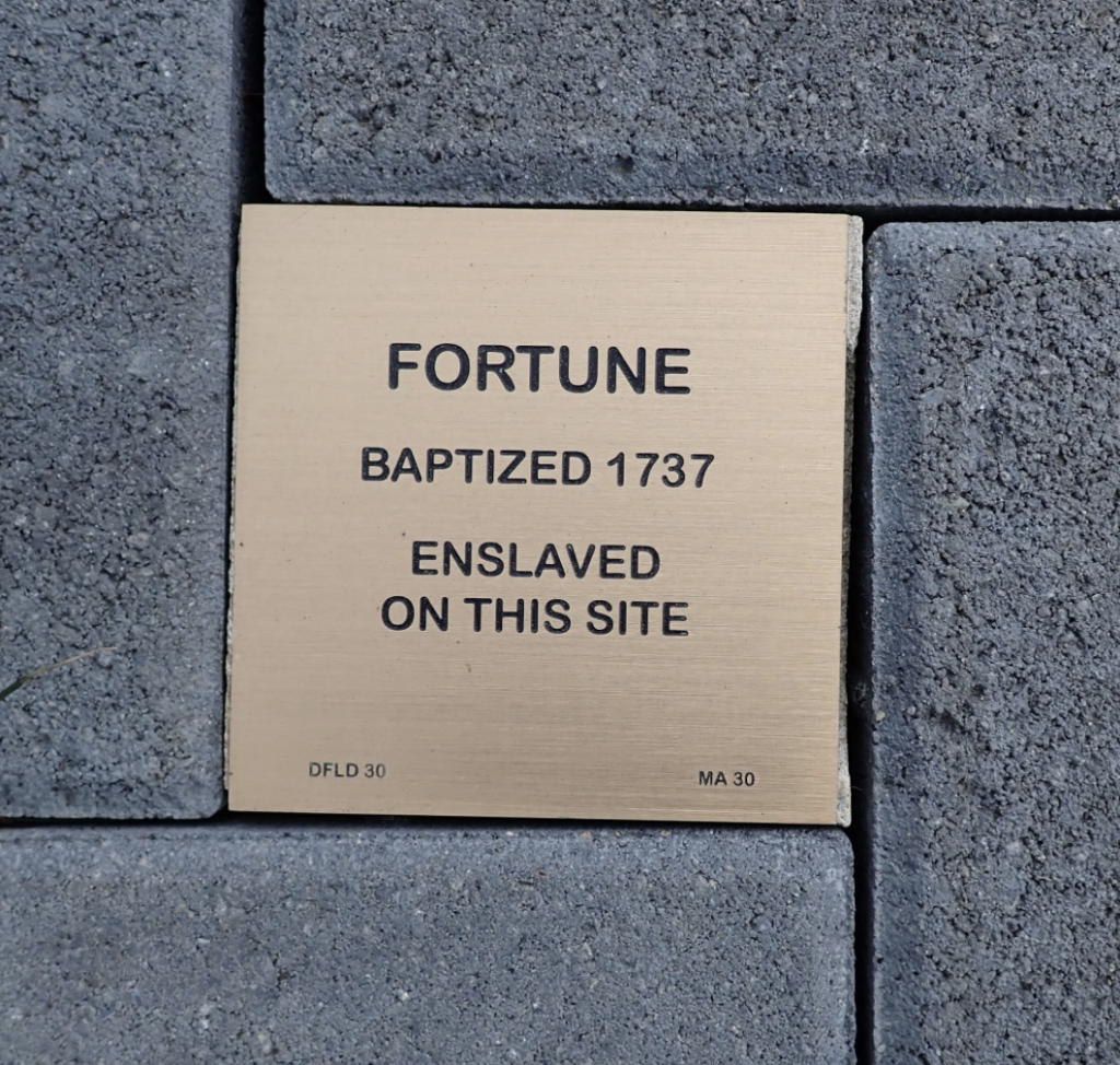 Memorial plaque for Fortune, baptized 1737, enslaved on this site, embedded in gray paving stones.