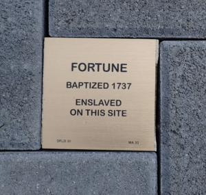 Memorial plaque for Fortune, baptized 1737, enslaved on this site, embedded in gray paving stones.