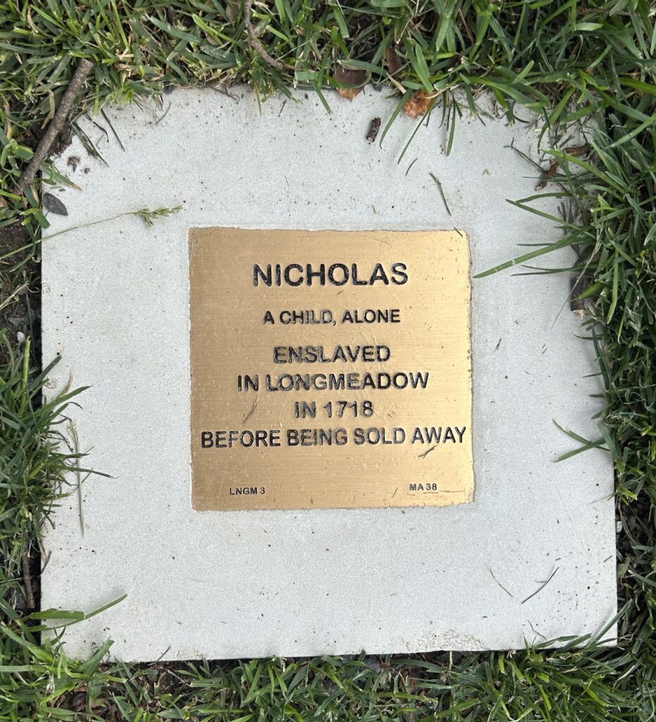 Memorial plaque honoring Nicholas, an enslaved child in Longmeadow, 1718, surrounded by grass.
