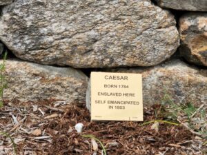 Historical marker for Caesar, born 1784, enslaved, self-emancipated in 1803, placed in front of a stone wall.