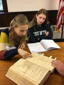 Two students at a table looking at, and identifying information, in an archival document.