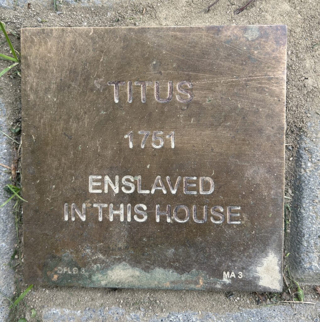 Bronze plaque reading Titus 1751 Enslaved in this house, set on the ground, for historical remembrance.