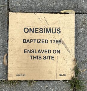 Plaque honoring Onesimus, baptized 1766, enslaved on this site. Historical marker on pavement.