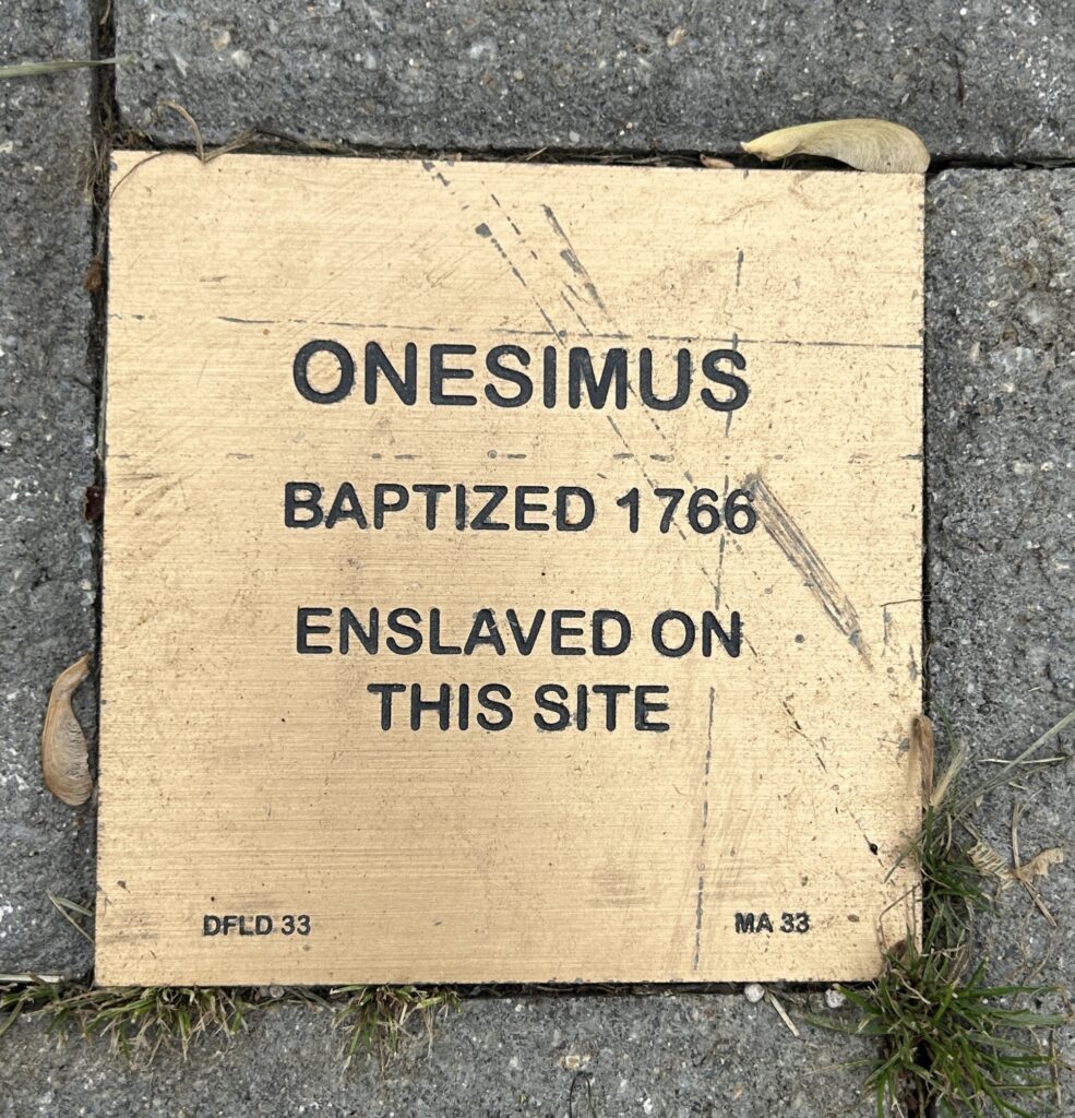 Plaque honoring Onesimus, baptized 1766, enslaved on this site. Historical marker on pavement.