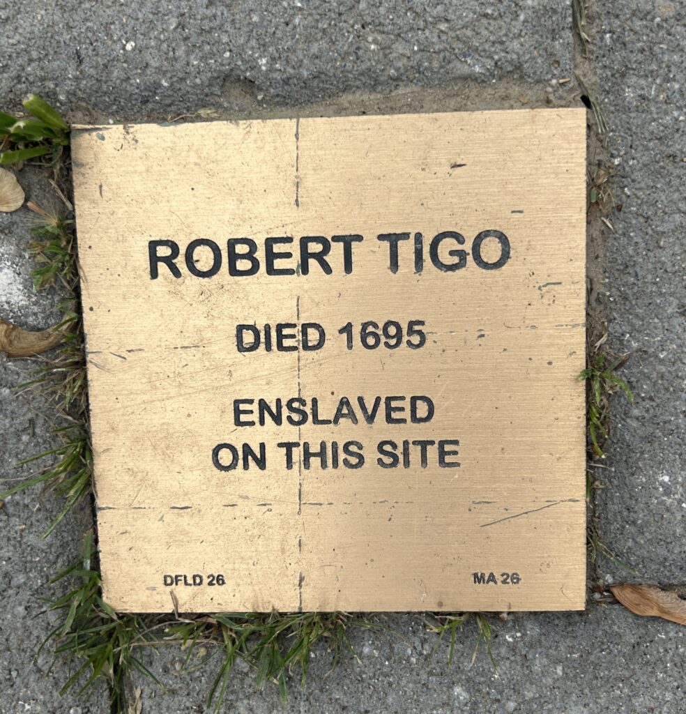Commemorative plaque for Robert Tigo, enslaved and died 1695, on site. A historical marker on pavement.