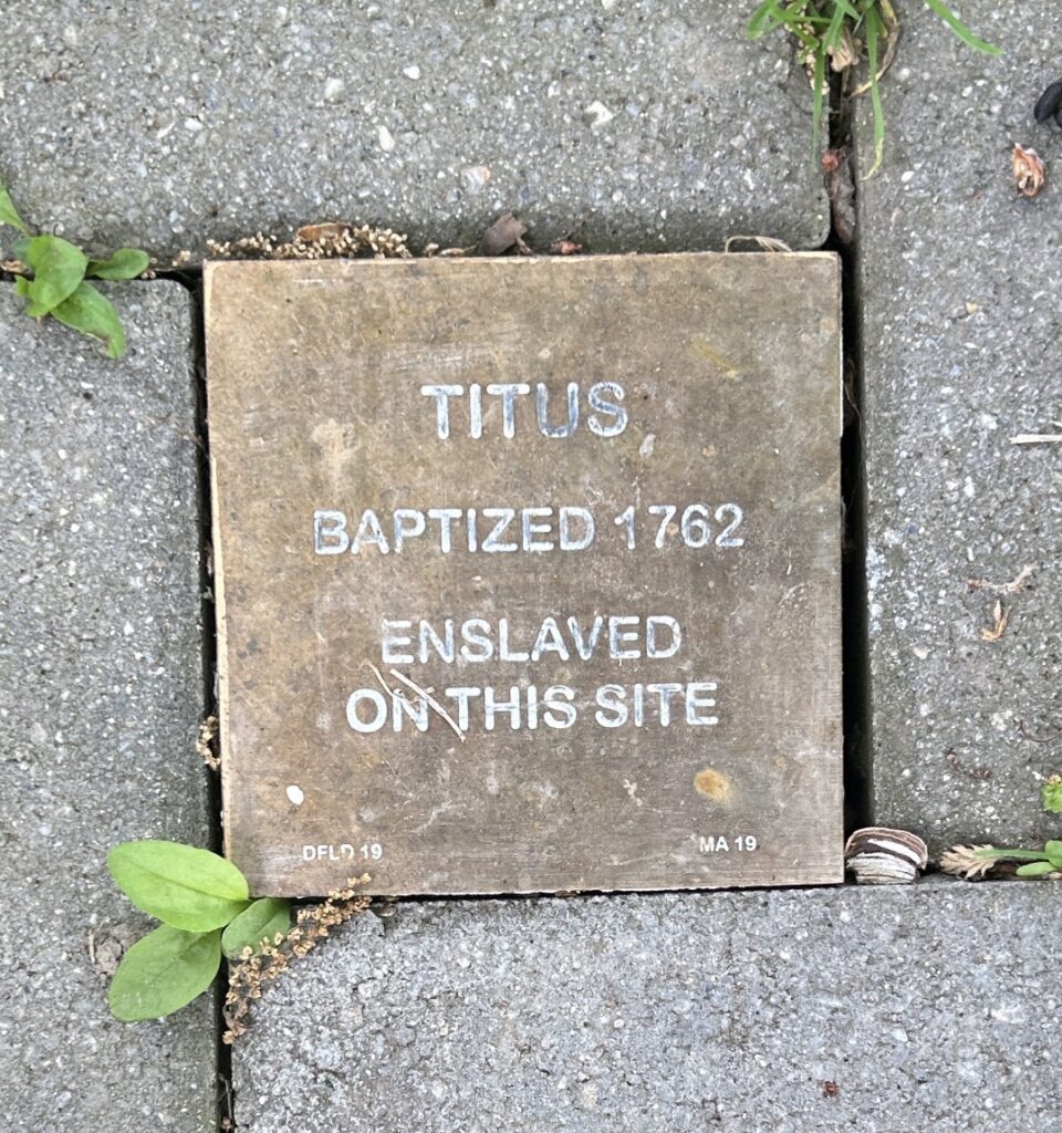 Commemorative plaque for Titus, baptized 1762, enslaved here. Historical site recognition.