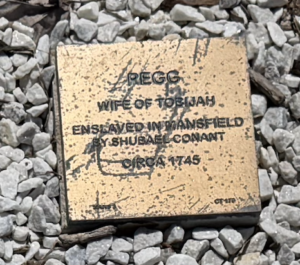 Memorial plaque for Pegg, enslaved in Mansfield by Shubael Conant, circa 1745, surrounded by gravel.