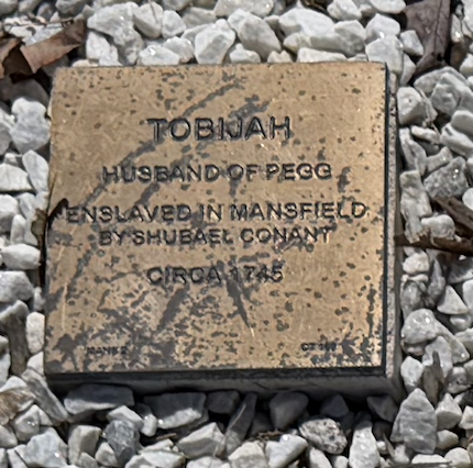 Historic marker for Tobijah, husband of Pegg, enslaved in Mansfield by Shubael Conant, circa 1745, on gravel background.