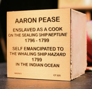 Wooden block with text: Aaron Pease, enslaved cook on Neptune (1796-1799), emancipated to Hazard (1799) in the Indian Ocean.