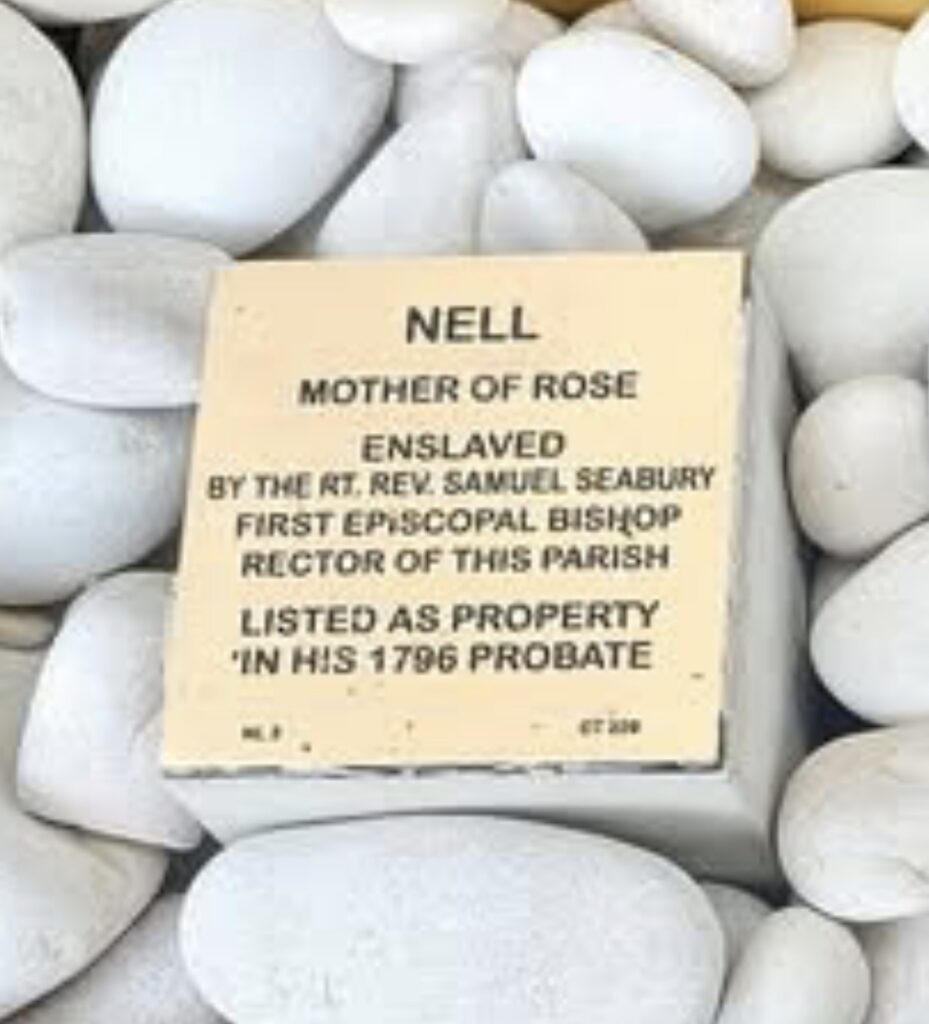 Plaque honoring Nell, enslaved by Bishop Seabury, surrounded by white stones, commemorating historical injustice.